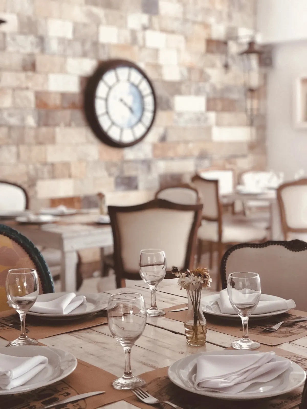 Mesa servida con copas junto a una pared de piedra con reloj en Pasta Rossa Adrogué