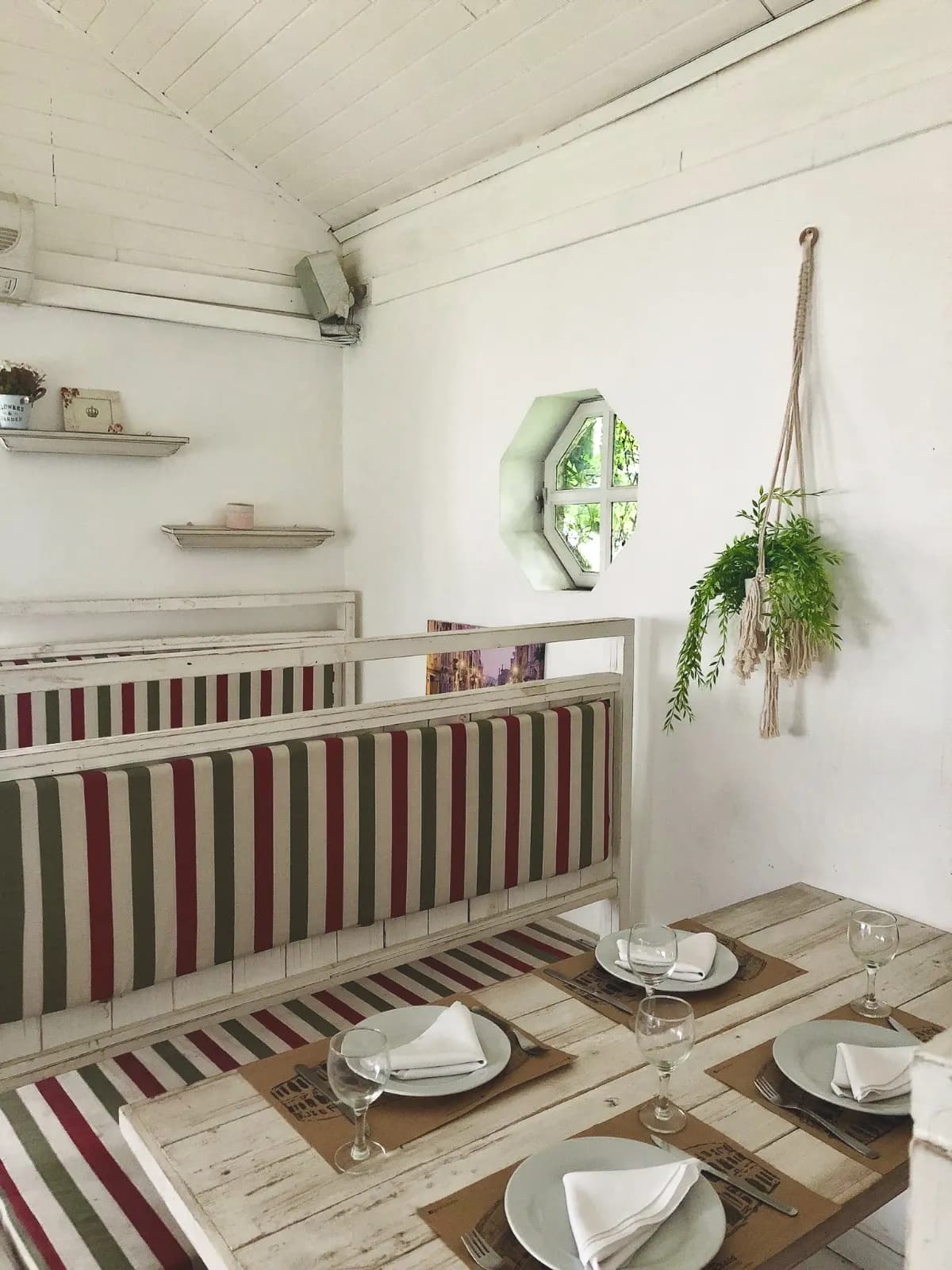 Rincón con banco a rayas, mesas de madera y plantas colgantes en Pasta Rossa Adrogué