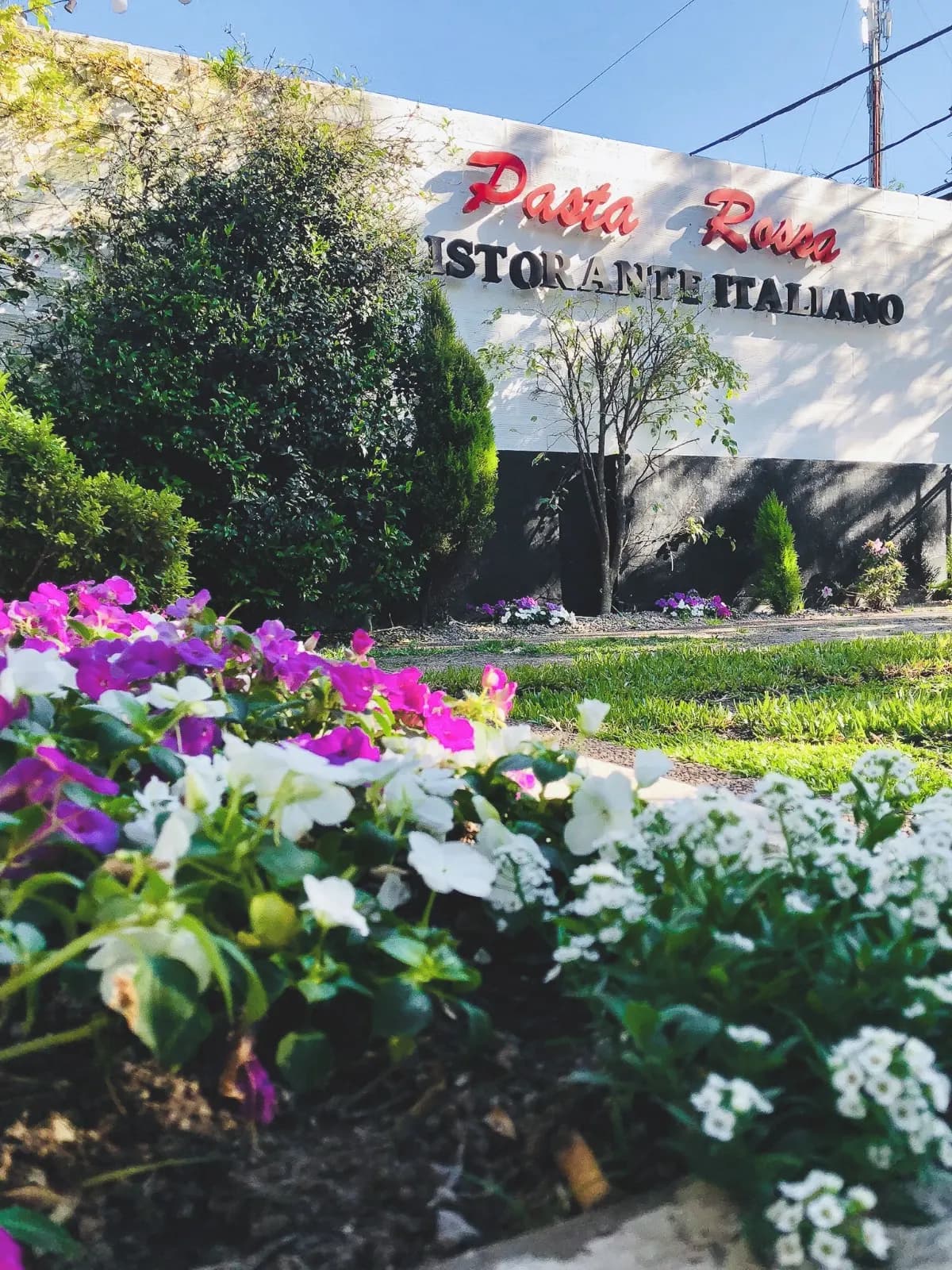Cartel de Pasta Rossa Ristorante Italiano sobre canteros con flores en Adrogué