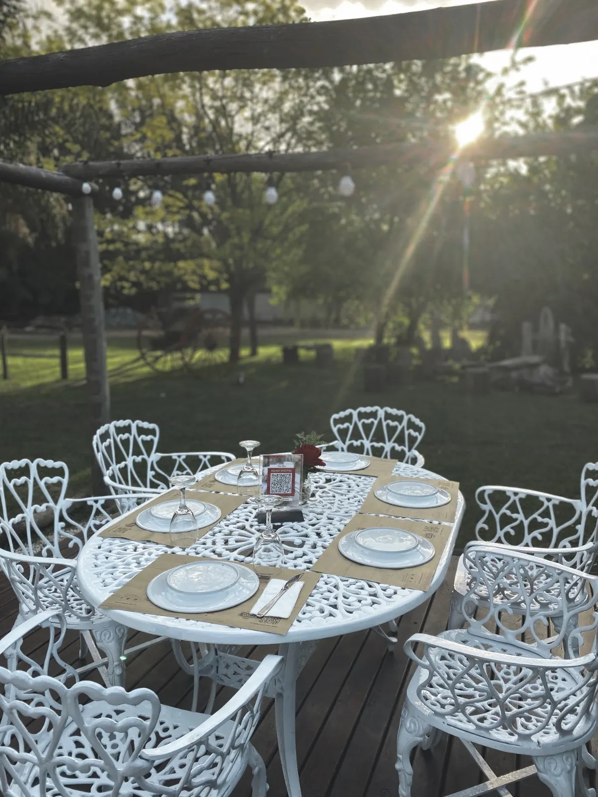 Mesa con sillas blancas de hierro en el jardín arbolado de Pasta Rossa Canning