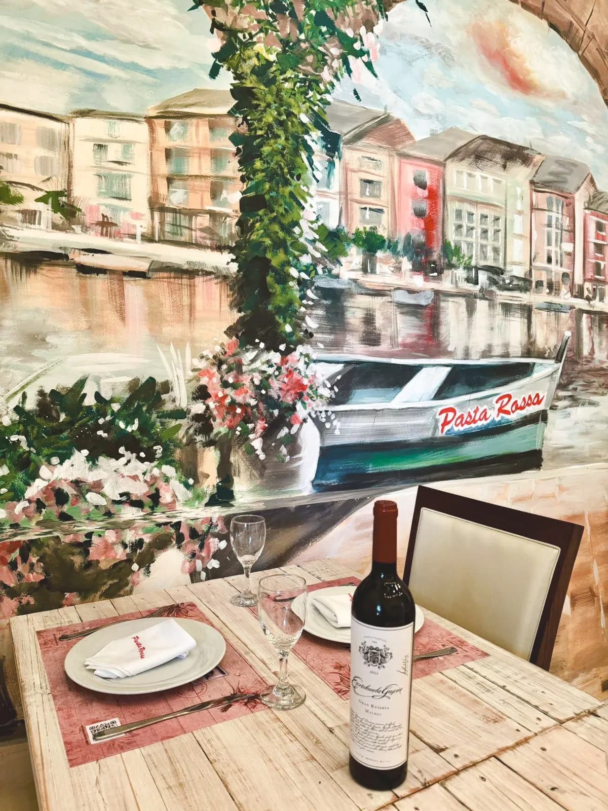 Mesa con vino frente a un mural de un canal veneciano en Pasta Rossa La Plata