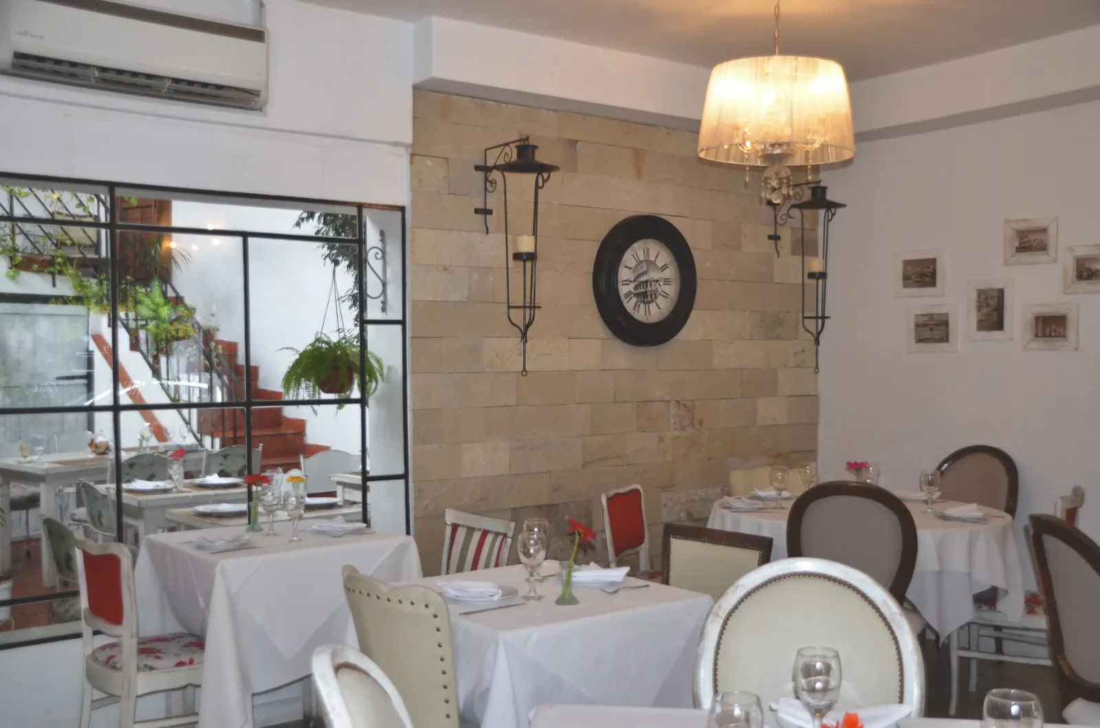 Salón con mesas de manteles blancos, reloj de pared y lámparas en Pasta Rossa Lomitas