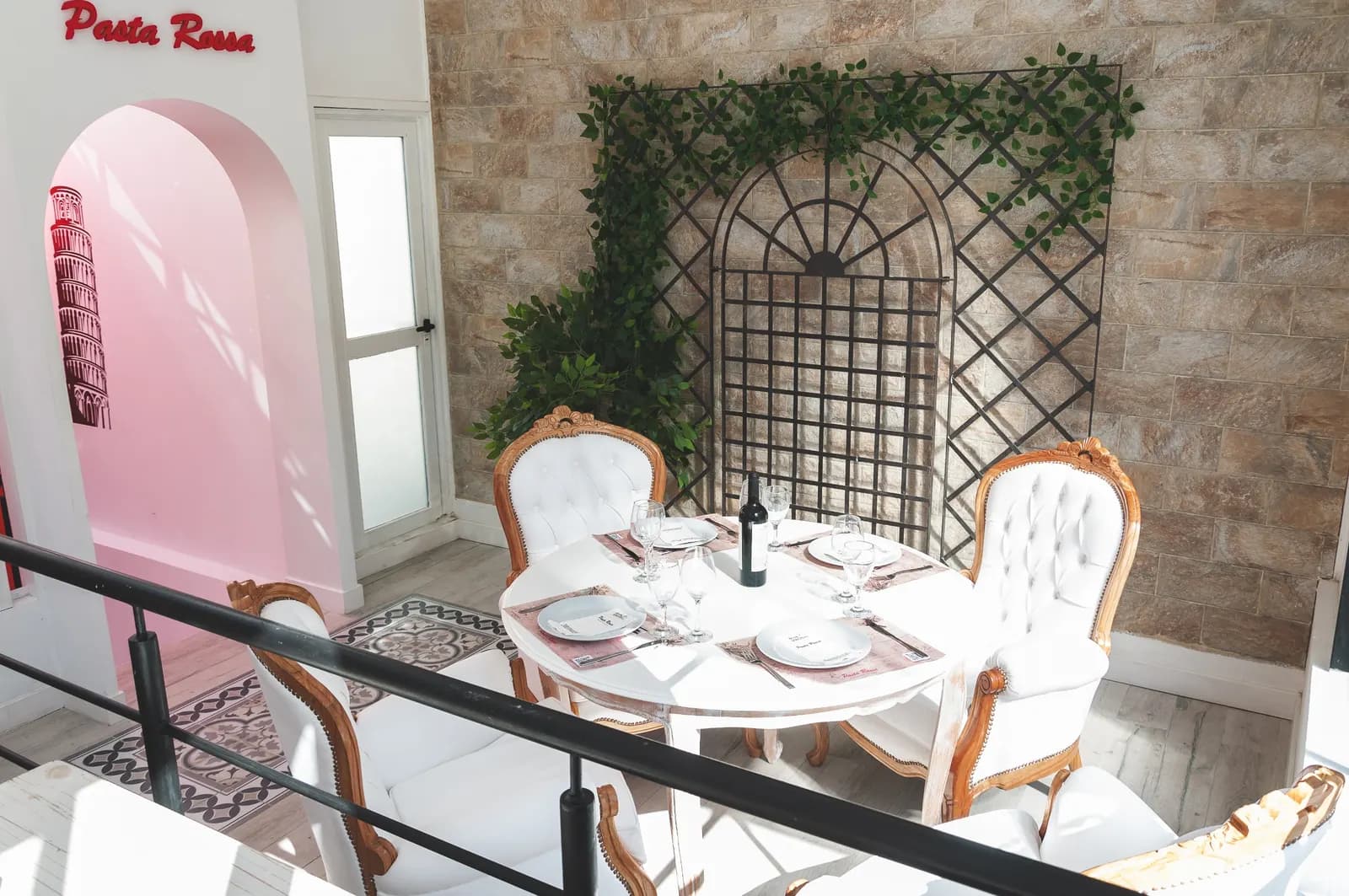 Mesa con sillas capitoné bajo un arco rosa y un enrejado con hiedra en Pasta Rossa Quilmes