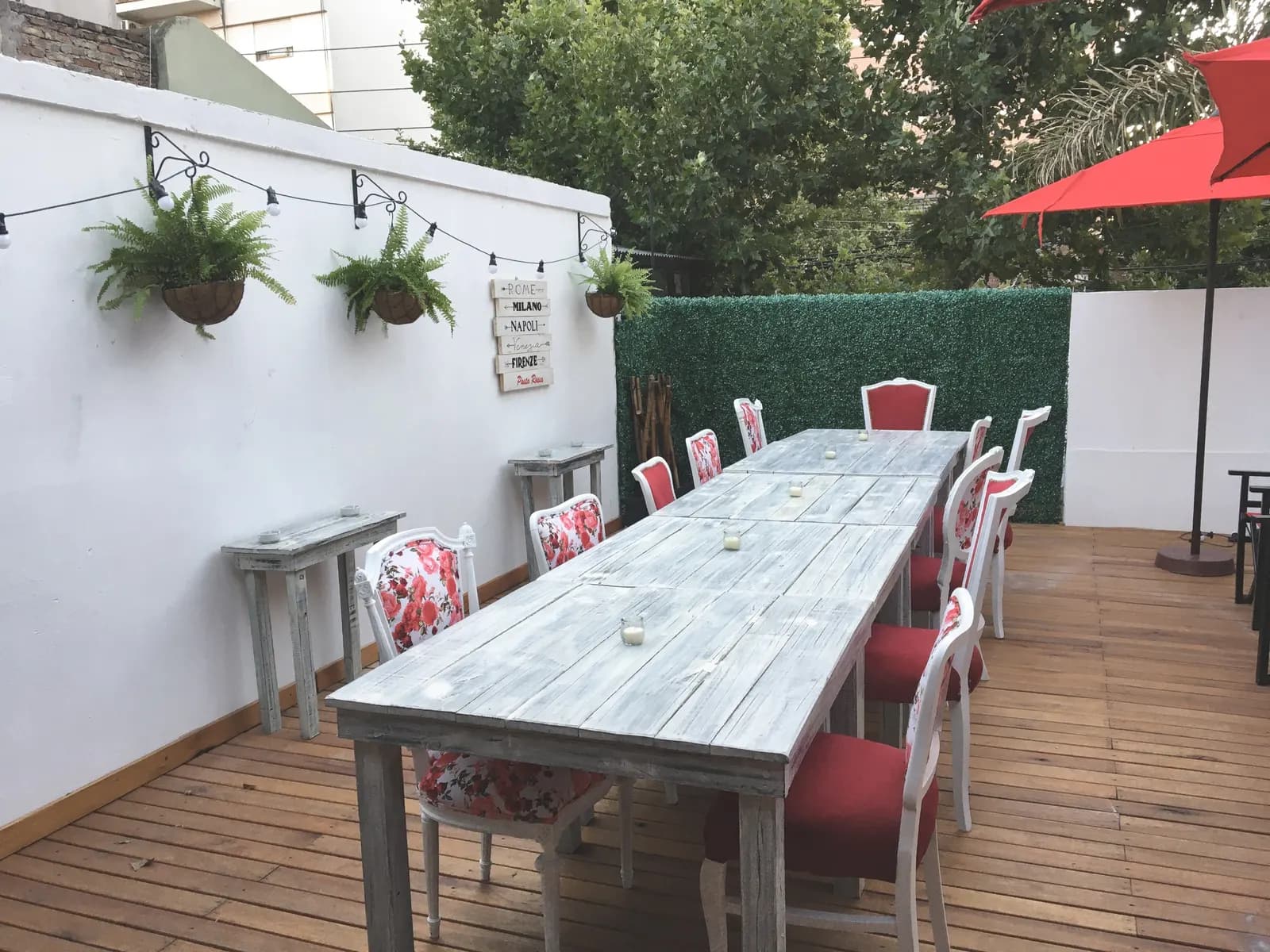 Terraza con mesa larga de madera y sillas floreadas en Pasta Rossa Ramos Mejía