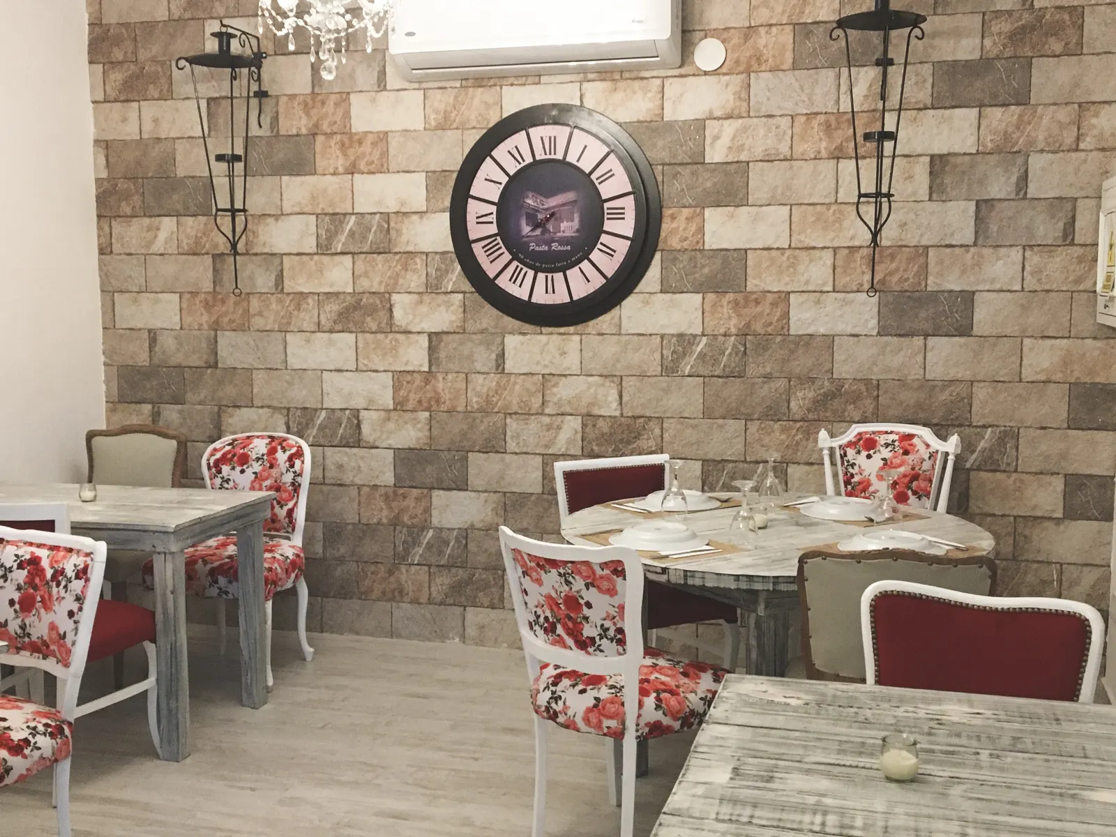 Salón con pared de piedra, reloj y sillas floreadas en Pasta Rossa Ramos Mejía