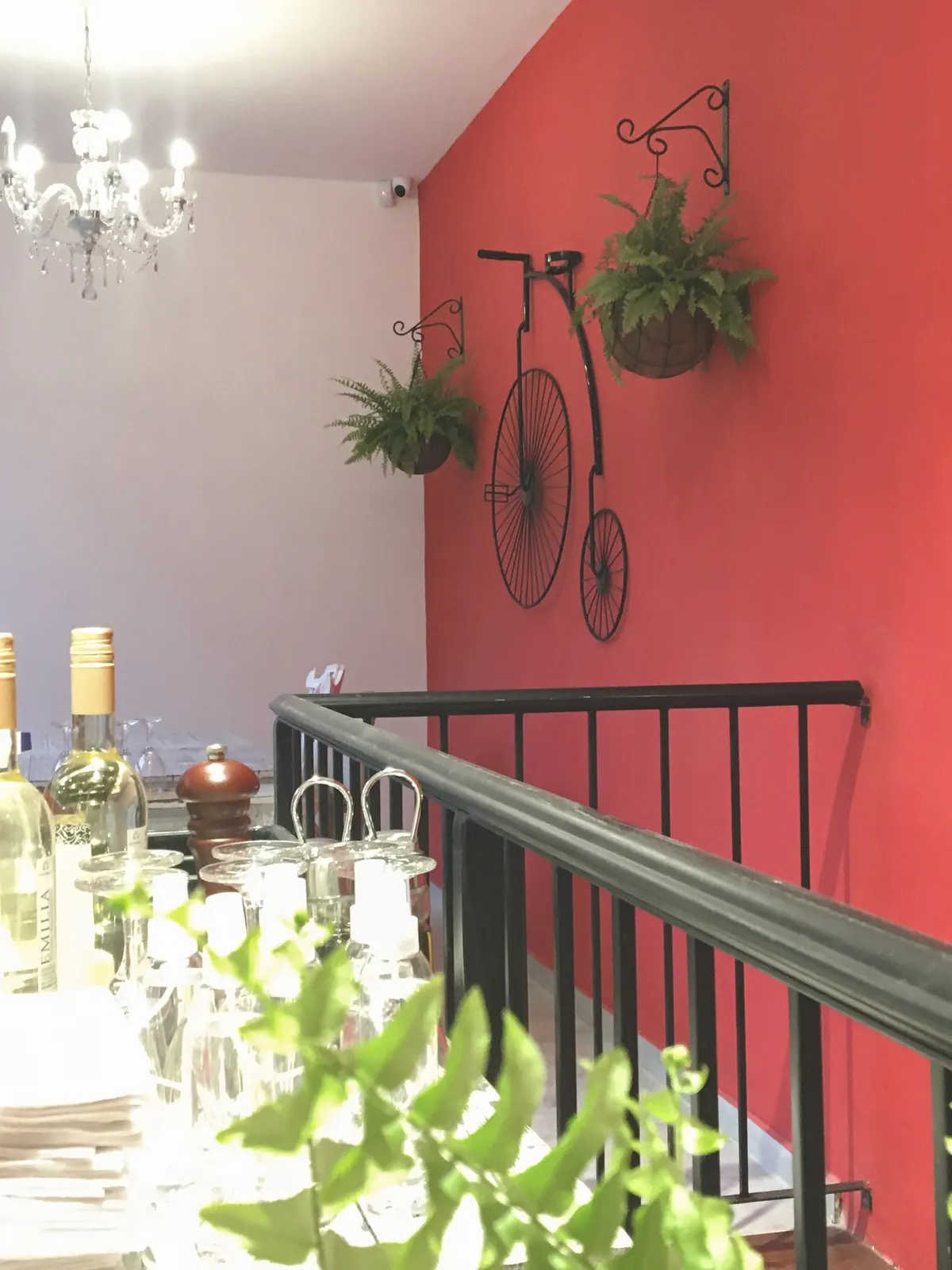 Pared roja con bicicleta antigua y plantas colgantes en Pasta Rossa Ramos Mejía